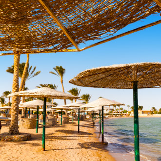 Zandstrand met parasols en palmbomen in Egypte