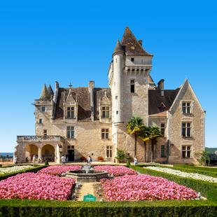 Kasteel bewondert roze bloemen in de tuin bij helderblauwe lucht, Dordogne, Frankrijk.