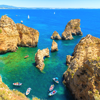 Rotsblokken in azuurblauw zeewater en vissersboten in Alvor in Portugal