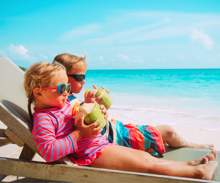 <p>Twee kinderen drinken uit een kokosnoot op een tropisch strand</p>