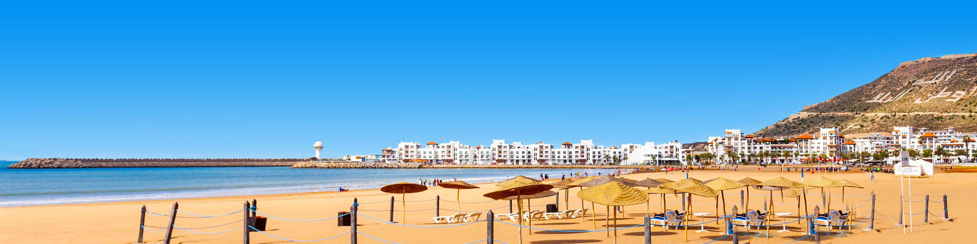 Goudgeel zandstrand met parasols, de zee en witte huizen op de achtergrond in Marokko