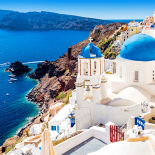 Witte huisjes met blauwe koepels in Oia, Santorini, op een klif boven zee met uitzicht op de caldera en diepblauw water.
