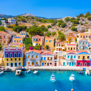 Gekleurde huisjes op Symi, dicht op elkaar gebouwd langs de haven, met felgekleurde gevels en boten in het blauwe water.
