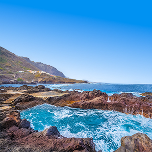 Natuurlijk lavazwembad in Garachico tussen donkere rotsen, met turquoise water en golven van de oceaan.