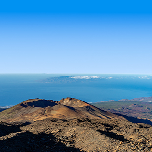 Uitzicht vanaf Pico Viejo over ruig vulkanisch terrein naar de oceaan en verre eilanden aan de horizon.