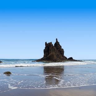 Rotsformatie bij Benijo Beach die uit zee oprijst, met golven en spiegeling in nat zand bij laag water.