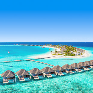 Luxe watervilla’s op palen boven felblauw zeewater, verbonden door een steiger met palmbomen en een klein eiland verderop.