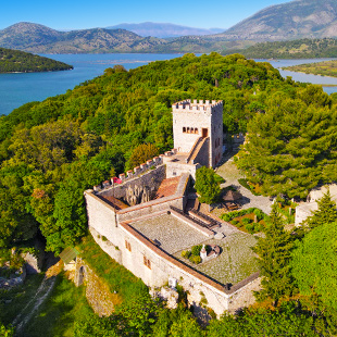 Oude stenen ruïnes van Butrint National Park in Albanië, omringd door groen en bomen, met resten van een antiek theater in een archeologisch landschap.