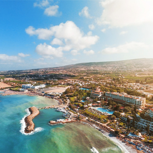 Strand bij Paphos op Cyprus met helderblauw water, lichte rotsformaties in zee en een zonnige kustlijn onder een strakblauwe hemel.