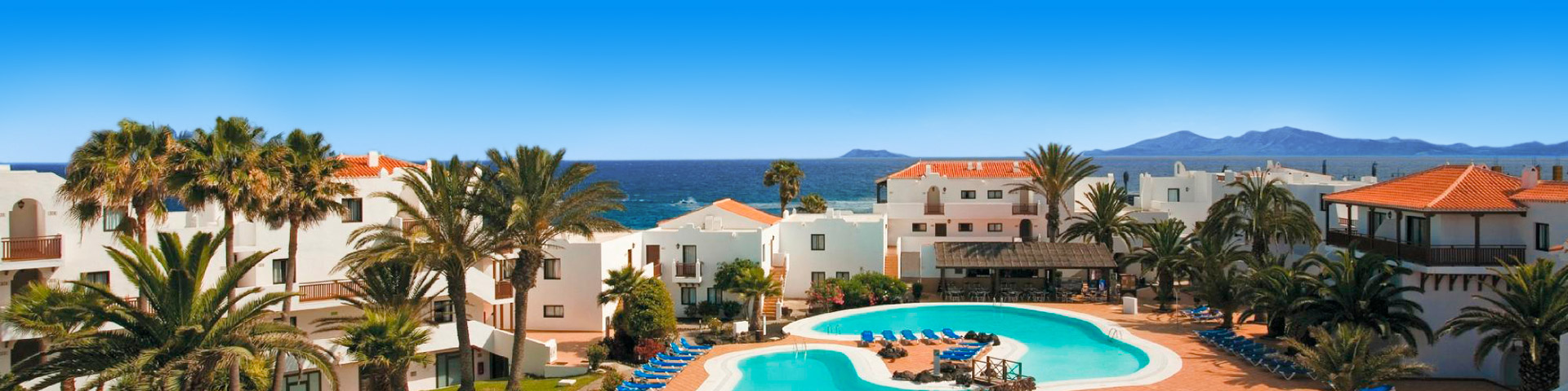 Hotel met witte kamers en oranje daken met 2 zwembaden en zee op de achtergrond