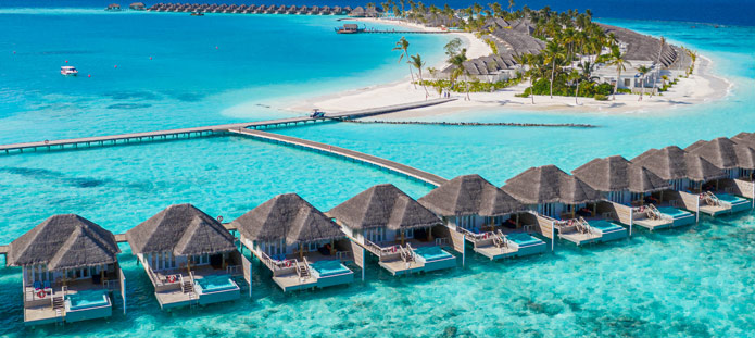 Helderblauwe zee bij de Malediven met waterbungalows op palen in zee met rieten daken