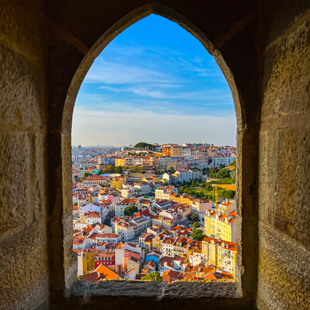 Uitzicht over Lissabon met kleurrijke daken en huizen, gezien door een stenen boog van Castelo de São Jorge onder een heldere blauwe lucht.