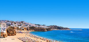 Geel zandstrand met ligbedjes en een blauwe zee in Portugal