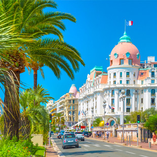 Promenade des Anglais in Nice met een lange boulevard langs de kust, palmbomen, strand en de helderblauwe Middellandse Zee.
