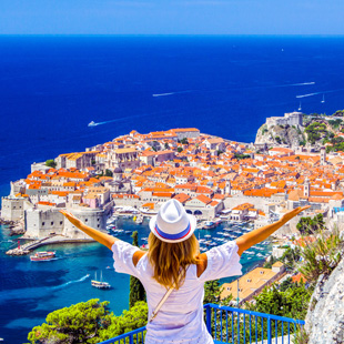 Uitzicht over de oude stad Dubrovnik met rode daken, historische stadsmuren en de Adriatische Zee op de achtergrond onder een heldere blauwe lucht.