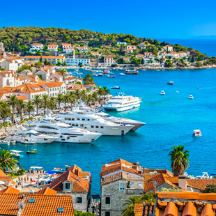 Uitzicht op de haven van Hvar met witte jachten, charmante gebouwen en heuvelachtig landschap onder een heldere hemel.