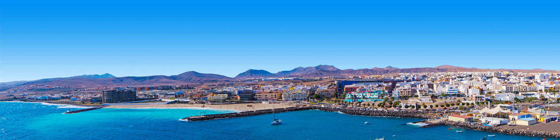 KPrachtige strand met blauwe zee en uitkijkend over een dorp en bergen op de Canarische Eilanden.