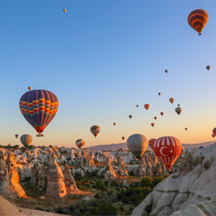 Kleurrijke luchtballonnen zweven bij zonsopkomst boven het rotslandschap van Cappadocië, met grillige rotspilaren en valleien onder een heldere lucht