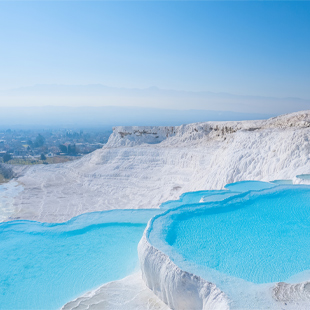Witte kalkterrassen van Pamukkale gevuld met helderblauw water, met uitzicht over het landschap en zachte bergen in de verte.