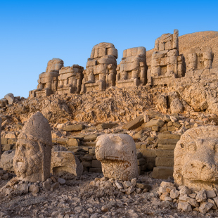 Monumentale stenen beelden en ruïnes op de berg Nemrut, verspreid over een rotsachtige helling onder warm avondlicht.