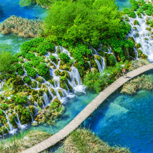 Toeristen wandelen over houten paden langs turquoise meren en groene natuur in Nationaal Park Plitvice in Kroatië.