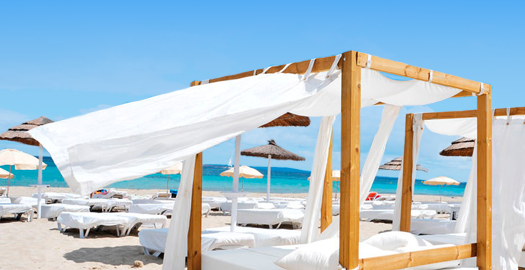 Loungebed met wapperende gordijnen op het strand