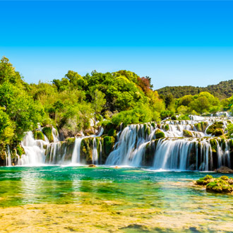 Indrukwekkende watervallen in Nationaal Park Krka stromen tussen groene vegetatie en rotsen, met wandelpaden voor bezoekers.